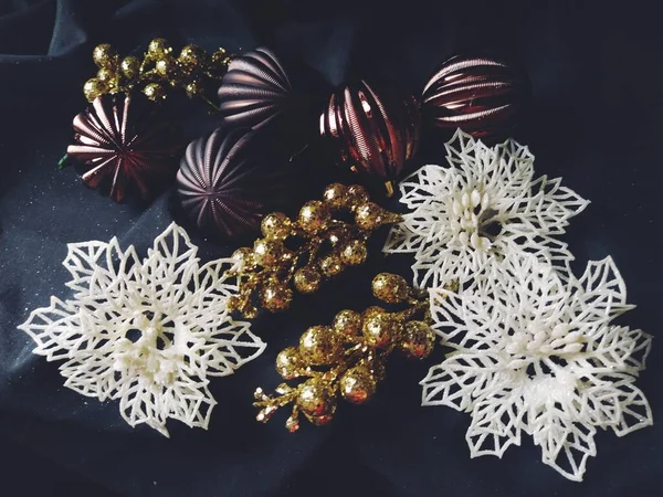 黒の背景に装飾、クリスマスの装飾や輝きを持つ新年とクリスマスのためのカード。茶色の光沢のある縞模様のボール、花と白い雪の結晶、果実と黄金の小枝 — ストック写真