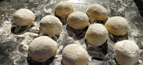 Morceaux ronds de pâte sablée pour faire des biscuits ou du pain d'épice. Petits pains crus ou des boulettes avec de la farine éparpillée autour sur fond noir — Photo