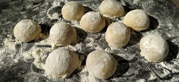 Morceaux ronds de pâte sablée pour faire des biscuits ou du pain d'épice. Petits pains crus ou des boulettes avec de la farine éparpillée autour sur fond noir — Photo