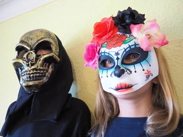 Barn klädda i svarta kostymer och läskiga halloween masker. Flicka i en mexikansk Kalaka Calavera mask. En pojke som bär en hemsk dödskallemask med svart huva. Alla helgons afton eller Alla helgons afton tema. — Stockfoto