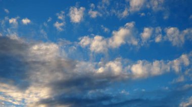 Güneş batarken göz kamaştırıcı canlı bulutlar. Gökyüzü, beyaz, sarı, turuncu, gri ve mavinin gölgeleriyle sakin bir atmosfer yaratır. Dramatik akşam gökyüzü. Bulutlar güneş ışınlarını yansıtır