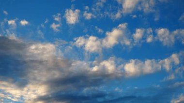 Güneş batarken çarpıcı ve canlı bulutların hızlanması. Gökyüzü beyaz, sarı, turuncu, gri ve mavinin tonlarıyla dönüşerek sakin bir atmosfer yaratır. Dramatik akşam gökyüzü. Bulutlar güneş ışınlarını yansıtır.