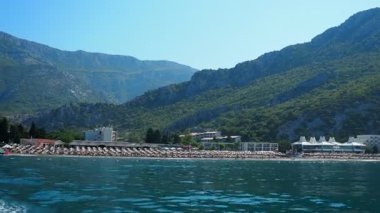 Canj, Karadağ 08.10.2025: Adriyatik Denizi 'nin berrak turkuaz sularının keyfini çıkarın. Plajları ve otelleri olan Balkan manzaralı bir turizm köyü. Yumuşak dalgalar etrafını saran dağların arasında kumsala çarpıyor..