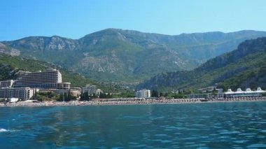 Canj, Karadağ 08.10.2025: Adriyatik Denizi 'nin berrak turkuaz sularının keyfini çıkarın. Plajları ve otelleri olan Balkan manzaralı bir turizm köyü. Yumuşak dalgalar etrafını saran dağların arasında kumsala çarpıyor.