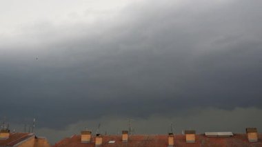 Uğursuz Kara Fırtına Bulutları Gökyüzünde Hızla Dalgalanıyor, Ağır oluşumları Kaos 'u serbest bırakmakla tehdit ediyor. Terracotta kaplamalı çatıda belirdiler, onu karanlık bir beklentiyle örttüler..