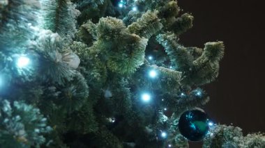 Noel ağacı ampuller ve çelenklerle parlar. Süslü Noel ağacı, Noel baloları. Kasaba meydanı şenlikli bir gecede. Şehirdeki aydınlanma. Kış havası. Yüksek kalite 4k görüntü