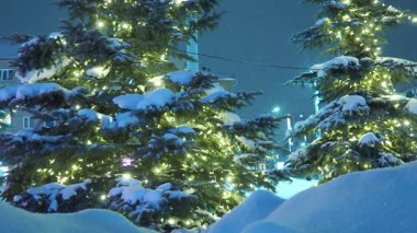Karlı şehir manzarası. Işıl ışıl ampullerden çelenkler içinde Noel ağaçları. Kışın kar yağışı. Kar yığınları ve kar yığınları. Noel havası. Sokakların şenlikli dekorasyonu. Xmas dekorasyonları