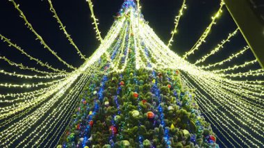 Çelenkleri parıldayan ışıklar, karanlıkta kar yağan büyük bir Noel ağacı. Yeni yıl ya da Noel için dekorasyon. Şehir aydınlanması. Xmas havası. Mutlu noeller. Şehir merkezi meydanı.