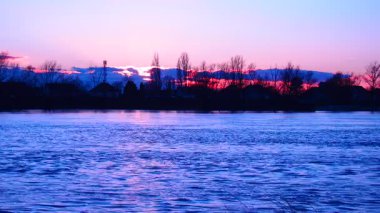 Sırbistan 'daki sakin Sava Nehri üzerinde güneş batarken meydana gelen büyülü dönüşüme tanık olun. Canlı pembe ve mavi renkler güzel bir şekilde harmanlanarak huzurlu ve huzurlu bir atmosfer yaratıyor.