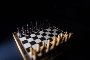 Satranç tahtasındaki satranç taşları koyu renkli ve beyaz bir ışıkla. Seçici odak