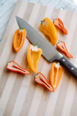 Çiğ organik mini kokteyl, kırmızı, turuncu ve sarı biber, tahta tahta ve bir bıçak ile ikiye bölünmüş. Dikey