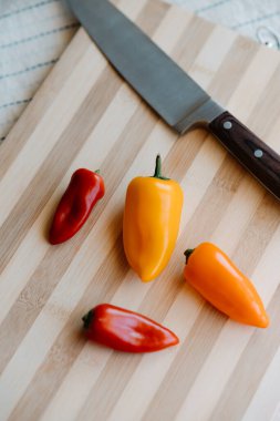 Tahta tahtaya çiğ organik küçük kokteyl, kırmızı, turuncu ve sarı biber ve bıçak koyun. Seçici odak