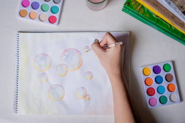 Beyaz bir masadaki eskiz defterinde renkli suluboya boyalar olan kadın el boyama balonu çizimi.