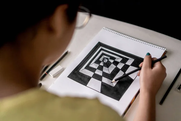 A woman making a perspective drawing with black and white fixings holding a pencil in her hand.