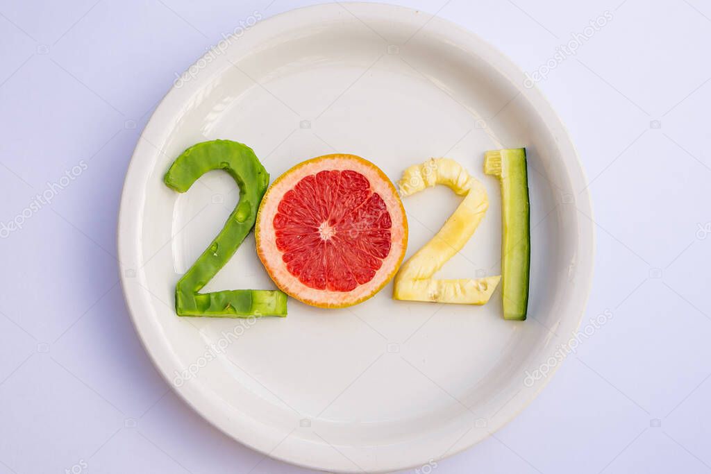 Delicious fruits cut in the shape of the new year 2021 in a white plate on a white table.