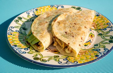 İçinde tavuk, ıspanak, avokado ve peynir bulunan nefis geleneksel Meksika dürümleri mavi bir masada el yapımı bir tabakta..