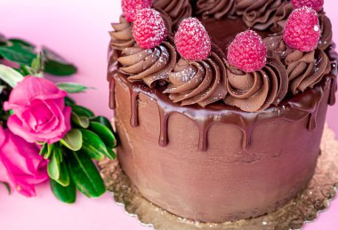 Çikolata kaplı lezzetli sevgililer günü pastası ve masanın üstünde pembe arka planda bir buket gülle kırmızı meyveler..