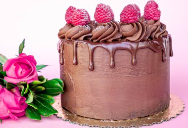 Çikolata kaplı lezzetli sevgililer günü pastası ve masanın üstünde pembe arka planda bir buket gülle kırmızı meyveler..