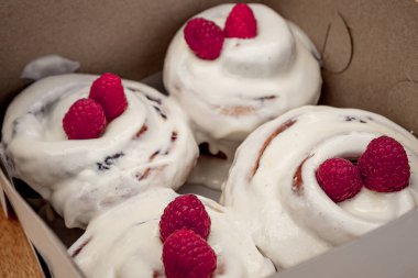 Bir kutunun içinde beyaz kremalı ve kırmızı meyveli nefis taze tarçın rolleri..