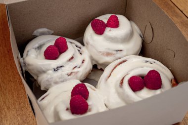 Beyaz kremalı ve kırmızı meyveli nefis tarçın rolleri tahta bir masada beyaz bir kutunun içinde..