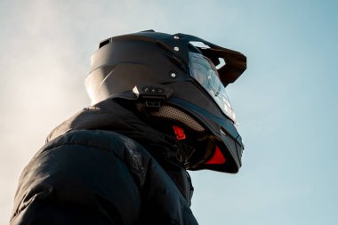 Çift amaçlı siyah kasklı, siyah ceketli, gökyüzüne doğru bakan bir motosikletli..