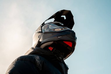 Çift amaçlı siyah kasklı, siyah ceketli, gökyüzüne doğru bakan bir motosikletli..