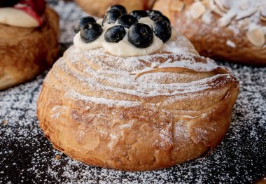 Üzerinde böğürtlen olan kruvasan hamuru, şeker serpiştirilmiş siyah bir masanın üzerine serpilmiş..