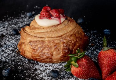 Üzerinde böğürtlen ve çilek olan peynirli kruvasan hamuru siyah bir masanın üzerine serpilmiş şeker konsepti serpiştirilmiş..