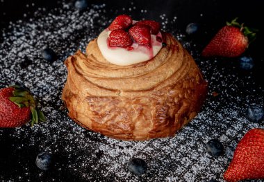 Üzerinde böğürtlen ve çilek olan peynirli kruvasan hamuru siyah bir masanın üzerine serpilmiş şeker konsepti serpiştirilmiş..