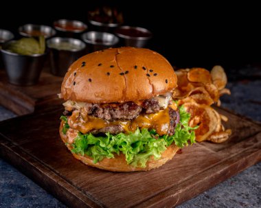 Ekmek, pastırma, Jack peyniri, çedar peyniri ve turşu soslu harika bir çift köfteli burger yanında da küçük bardakta soslu patates cipsi..