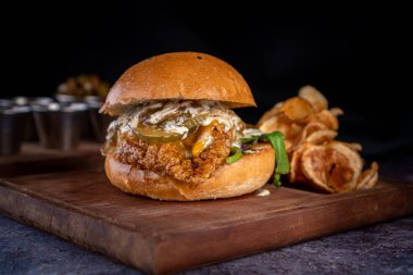 Ekmek, sos, karamelize soğan, ıspanak ve turşu ile iştah açıcı tavuk burger yanında patates kızartması ve en alttaki küçük bardakta sos..