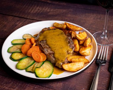 Meksika soslu iştah açıcı bir parça et kabağı, havuç ve patates yanında çatal ve bıçakla kırsal bir masada servis edilen beyaz bir tabakta servis ediliyor..