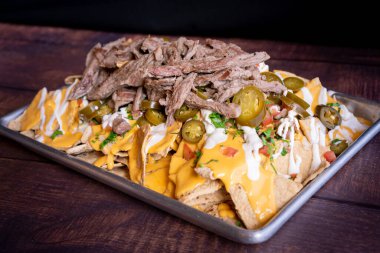 Exquisite nachos with meat, chili, cheese, tomato, cilantro and cream served on a tray on a rustic style table.