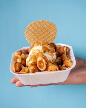 Karamelli elma, karamel ve vanilyalı dondurma ile nefis köpüklü waffle. Mavi arka planı olan bir el tarafından tutulmuş..