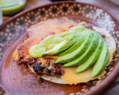 Meksika usulü altın peynirli nefis, katı sığır eti, yanında da avokado ile yeşil sos, kil bir tabakta servis edilir..