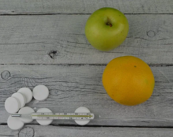桌上放着一个苹果 上面放着一个桔子和一个装有药丸的温度计 — 图库照片