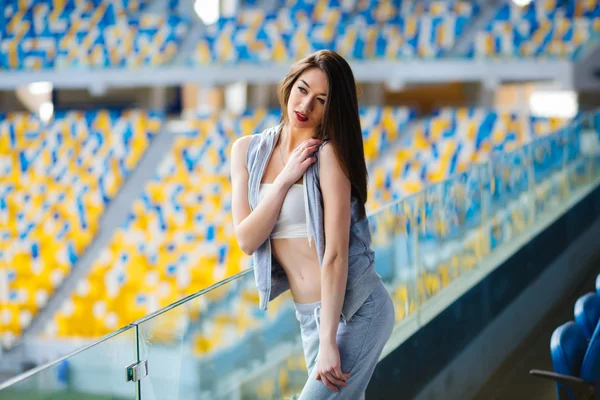 Schöne sportliche athletische Mädchen in kurzen Hosen und ärmellosem Hemd, die sich zwischen blauen Sitzen auf einem Stadion während des Abendlaufs im Freien auf dem Universitätscampus-Stadion strecken — Stockfoto