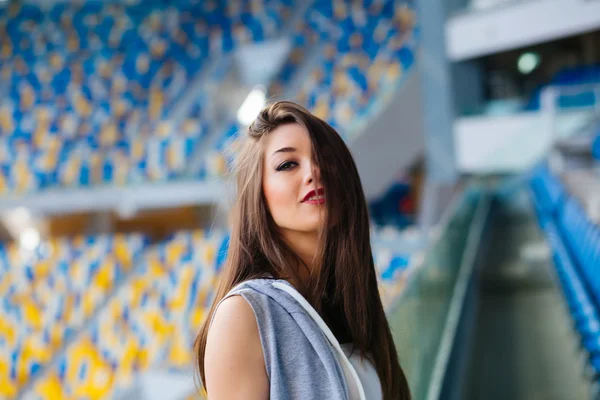 Beautiful sporty athletic girl in shorts and sleeveless shirt stretching between blue seats on a stadium during evening run outdoors at university campus stadium — Stock Photo, Image