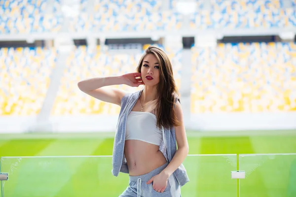 Όμορφο σπορ αθλητικό κορίτσι με σορτς και αμάνικο πουκάμισο εκτείνεται μεταξύ μπλε καθίσματα για ένα γήπεδο κατά τη διάρκεια της βραδιάς τρέξει σε εξωτερικούς χώρους στο γήπεδο της πανεπιστημιούπολης του Πανεπιστημίου — Φωτογραφία Αρχείου
