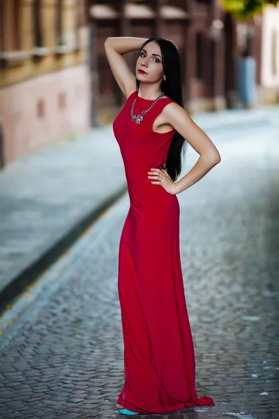 Hermosa joven en vestido largo rojo posando cerca de paredes de ladrillo rojo —  Fotos de Stock