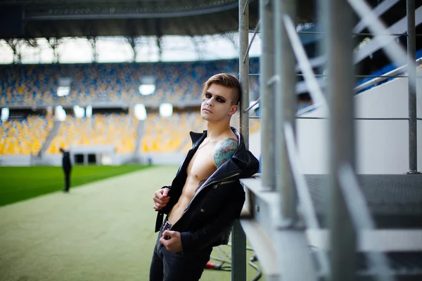 Hombre joven en chaqueta pecho desnudo, de pie en el estadio, con th — Foto de Stock