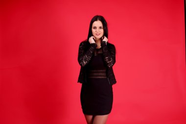 Moda bir zarif siyah elbisenin içinde muhteşem genç kadını vurdu. Kırmızı zemin üzerine.