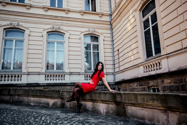 Belle fille brune dans une robe rouge avec de longs cheveux sains, créant sur le fond de la vieille dame du bâtiment, Lviv — Photo