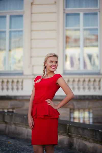 Street fashion concept: Portrait of a beautiful young woman wearing a red dress walking in the city. Old architecture background — Stock Photo, Image