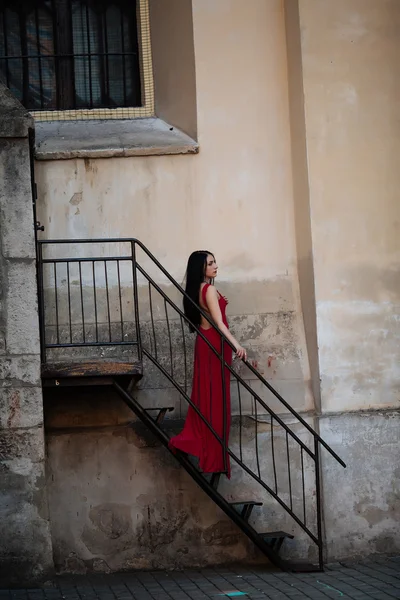 Mladá žena krásná a velmi elegantní v dlouhé černé večerní šaty pózuje na schodech, Foto zezadu — Stock fotografie