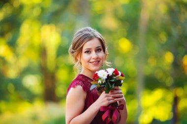 Pembe elbiseli, elinde bir buket çiçekle parkta poz veren genç ve güzel bir kadın.