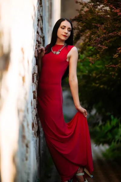 Retrato de beleza de moda. Mulher bonita com cabelo encaracolado vestindo um vestido vermelho moda, de pé contra a parede, fechou os olhos — Fotografia de Stock