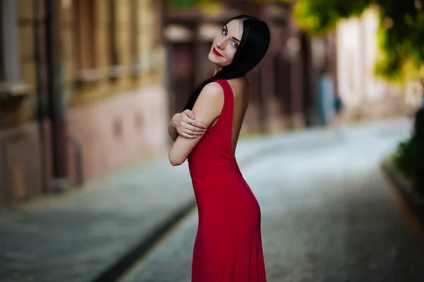 Cheerful young brunette in a red dress posing on the street in L — Stock Photo, Image