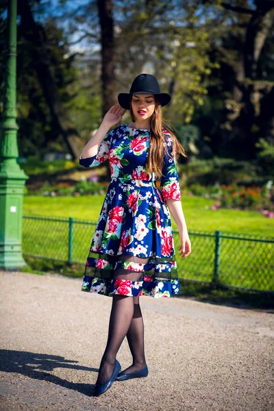 Pretty slim girl with long hair in an elegant hat in a simple flowered dress walking in the summer in the park at sunset — Stock Photo, Image