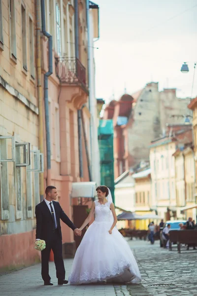 Fotografia de casamento. Noiva e noivo andando na cidade. Casamento casal abraçando e olhando um para o outro. A segurar o buquê. Ao ar livre, corpo inteiro — Fotografia de Stock